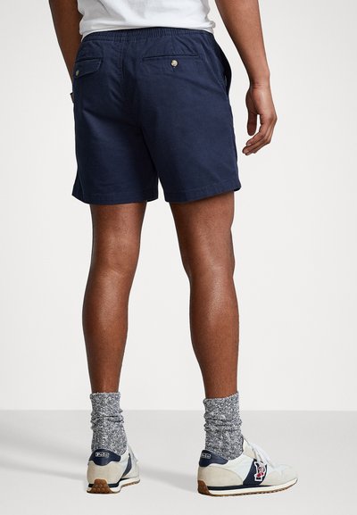 Shorts in cotone blu navy con vita elastica, due tasche posteriori e una vestibilità comoda, abbinati a sneakers bianche e calzini grigi a righe.