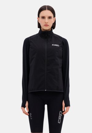 Woman wearing a black zip-up sleeveless vest and long-sleeve top, with black fitted shorts featuring "cep" and "75" branding.