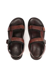 Pruunid nahast sandaalid avatud disainiga, reguleeritavate rihmadega, mustade detailidega ja pehmendatud tald. Nähtav kaubamärgi nimi "Kazar".