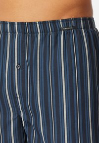 Gestreepte boxershort in marineblauw, lichtblauw en wit. Gemaakt van zachte stof met een elastische tailleband en een enkele knoopdetail.