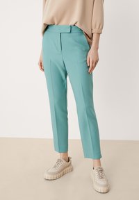 Miękkie, turkusowe spodnie w tapered z przodu z fałdami, zestawione z beżowymi sneakersami na platformie o teksturowanym wykończeniu.