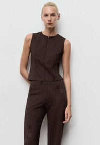 Bruine pinstripe mouwloze top met hoge hals, gecombineerd met bijpassende slim-fit broeken. Soepele stof, gestructureerd ontwerp en subtiele afwerking.