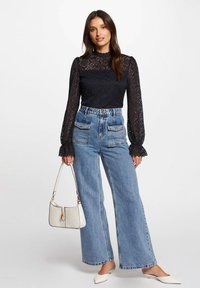 Top in pizzo navy con maniche lunghe, abbinato a jeans a vita alta di un azzurro chiaro e a gamba ampia. Scarpe bianche a punta e una borsa crema.