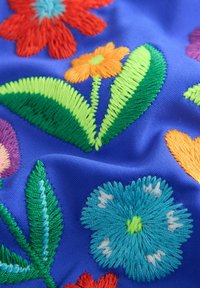 Broderad tyg med färgglada blommönster på en livlig blå bakgrund. Texturerad med tråddekorationer i röd, orange, grön och blå.