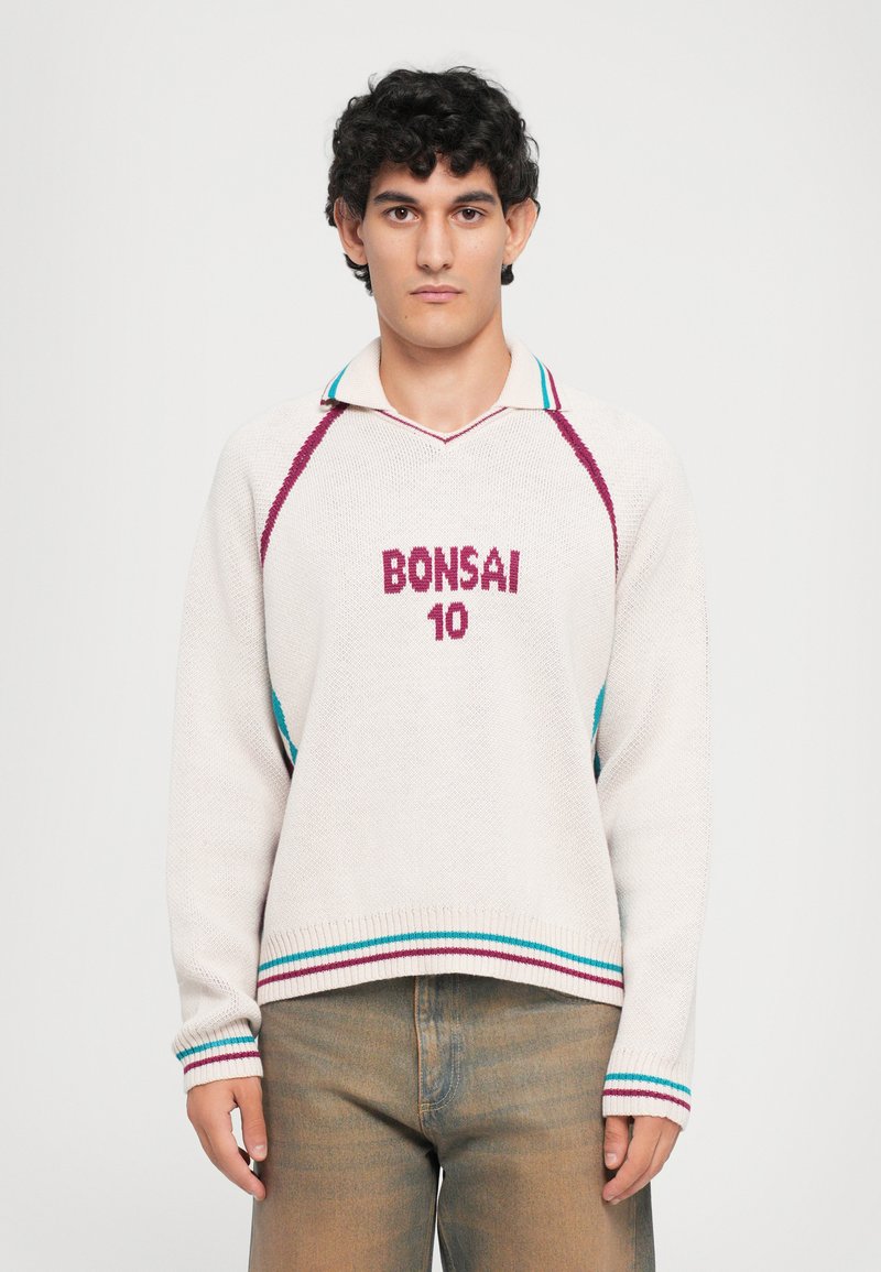 Pull en tricot crème avec un col en V, présentant des rayures contrastées turquoise et bordeaux et brodé "BONSAI 10" sur le devant. Manches raglan.