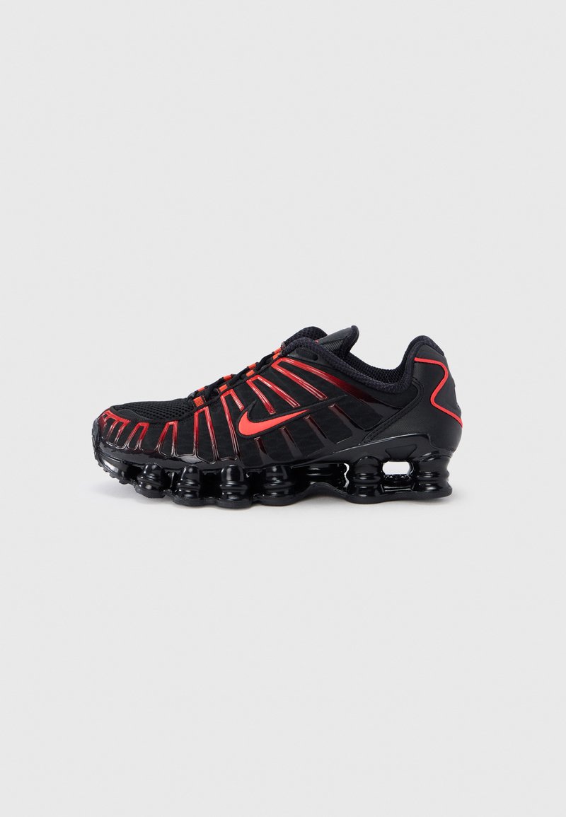 Black athletic shoes with red accents, featuring a textured mesh upper, a unique wavy design, and a molded cushioned sole.