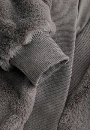 Graue Fleecejacke mit weichemFellkragen. Verfügt über gerippte Bündchen und eine Texturvariation zwischen glatten und plüschigen Abschnitten.