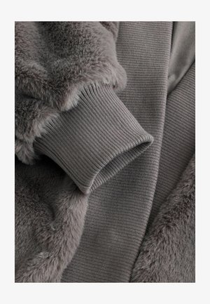 Graue Fleecejacke mit weichemFellkragen. Verfügt über gerippte Bündchen und eine Texturvariation zwischen glatten und plüschigen Abschnitten.