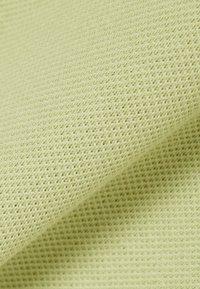 Lichtgroene stof met een fijn, textuurrijk breipatroon, close-up weergegeven met een zachte plooi die zachte schaduwen creëert.