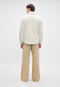 Beige fleecejakke med krage og knappede mansjetter, parret med vide beige bukser. Myk tekstur og avslappet passform.