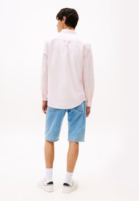 Lichtroze blouse met lange mouwen, gecombineerd met blauwe denimshorts. De outfit wordt compleet gemaakt met witte sneakers en crew-lange witte sokken.