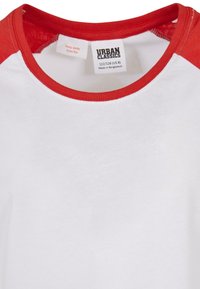 Rød og hvit raglan t-skjorte med rund hals. Laget av bomull, med rød krage og ermer, samt en vaskeanvisning inni.