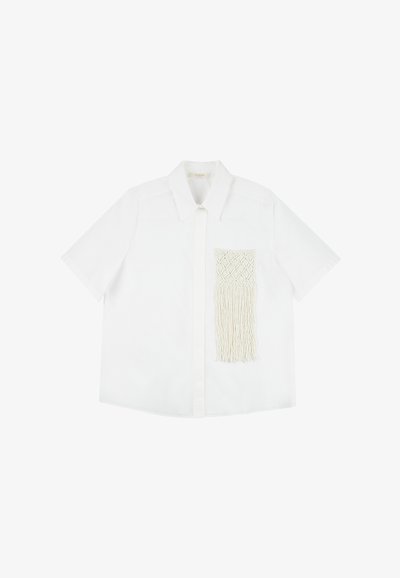 Camicia bianca a maniche corte con colletto a punta e tasca in macramé testurizzata con dettagli di frange sul lato sinistro.