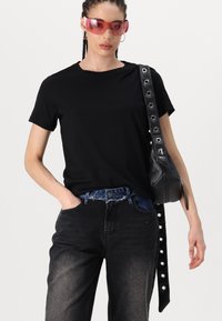 Sort bomulds t-shirt med korte ærmer, parret med mørk denim jeans. Accessoriseret med en sort lædertaske med metalhardware og nitter.