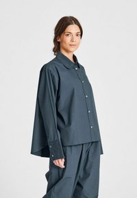 Camicia oversize di un blu scuro, con chiusura a bottoni davanti, un ampio colletto e maniche con risvolto. Realizzata in tessuto leggero, presenta una vestibilità comoda.