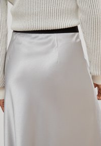 Falda de satén plateado con una textura suave, talle alto y una sutil abertura lateral; combinada con un suéter de punto blanco con rayas oscuras.