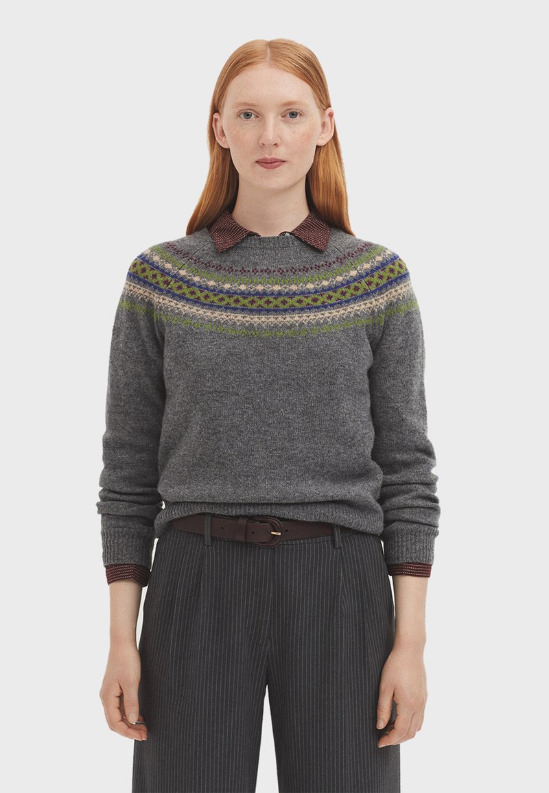 Pull gris en tricot avec un empiècement à motifs multicolores, associé à une chemise à col bordeaux et un pantalon à rayures.