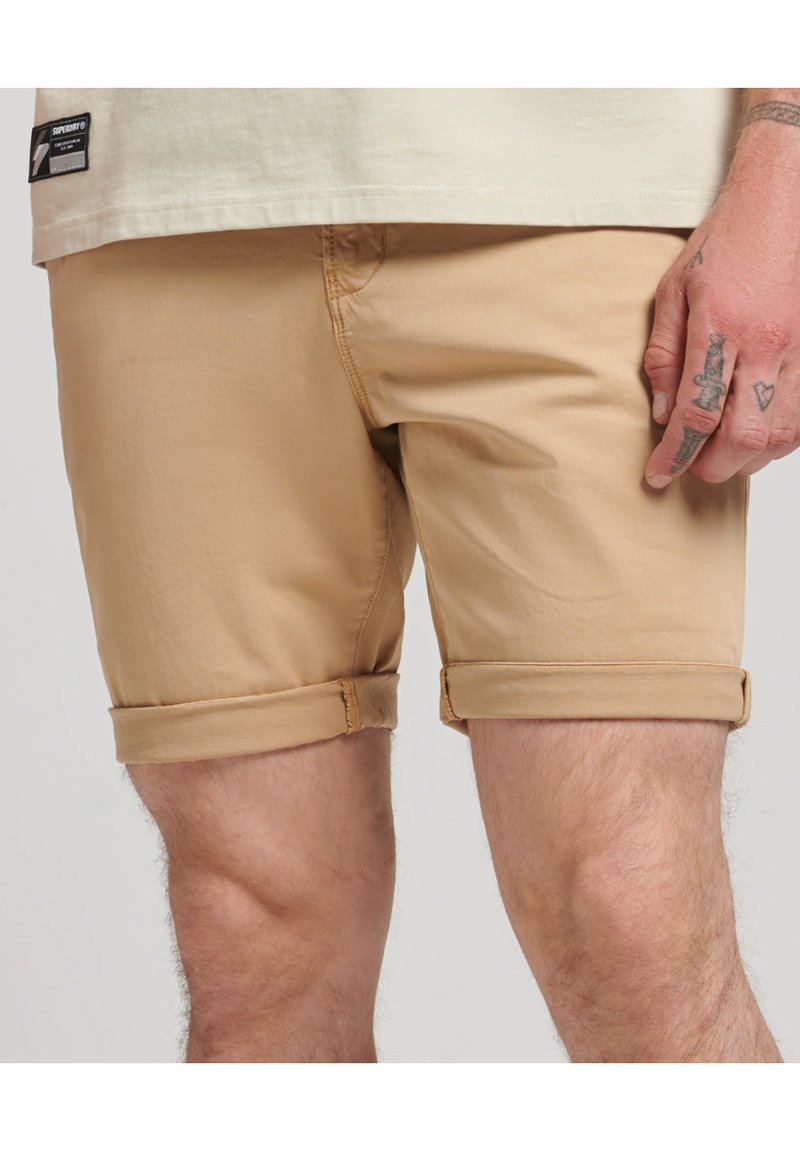 Beige kokvilnas šorti ar apgrieztu apakšmalu, ar taisnu priekšpusi, sānu kabatām un redzamām šuvju detaļām.