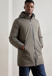 Lightweight gray-green puffer jacket with a hood, front zipper, and side pockets. Features a smooth texture and minimalist design.