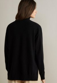 Svart ulltröja med hög krage, sänkt axlar och ribbade mudd. Baksidan har en avslappnad passform och en slät, mjuk textur.