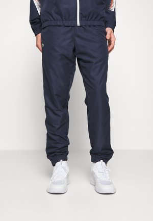 Pantalons de running légers bleu marine avec une taille élastique et des poignets, fabriqués dans un matériau lisse et résistant à l'eau.
