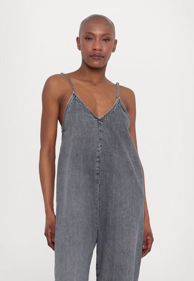 Combinaison en denim gris avec bretelles fines, décolleté en V et détails de couture subtils. Coupe ample et texture lisse, convient pour un usage décontracté.