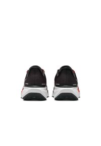 Chaussures de sport noires avec un dessus en mesh texturé, semelle blanche et accents rouges, dotées d'un talon rembourré et d'une semelle extérieure orientée traction.