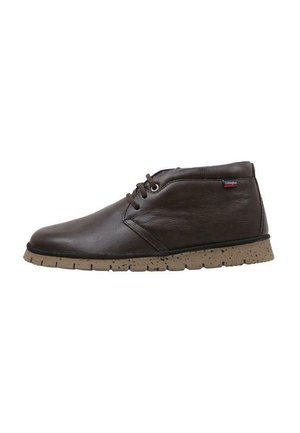 Botas chukka de cuero marrón con punta redondeada, costuras mínimas y suela de goma beige con manchas. Diseño simple de cordones.