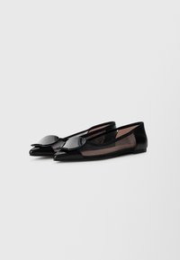 Des chaussures plates noires avec un bout pointu, fabriquées dans un mélange de maille et de matériau lisse, avec un accent noir brillant à l'avant.