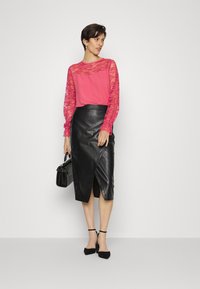 Top de renda rosa de mangas longas com corpete sólido, combinado com uma saia preta de couro de cintura alta com design envolvente e fenda. Bolsa preta.