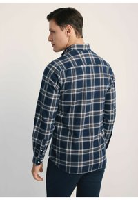 Koszula flanelowa w niebieską kratę z długim rękawem. Posiada białe i jasnoniebieskie kratki; mankiety na guziki, klasyczny kołnierz oraz zaokrąglony dół.