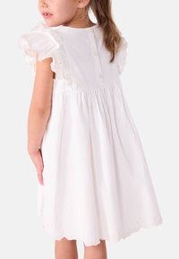 Άσπρο βαμβακερό φόρεμα με μανίκια με βολάν, κλείσιμο με κουμπιά στο πίσω μέρος και φούστα με πιέτες. Η διακοσμητική λοξή ραφή στο τελείωμα προσθέτει υφή.