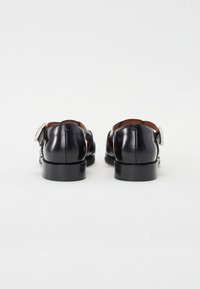 Black leather shoes featuring a smooth texture, rectangular buckle detail, and a low, rounded heel. Designed with a sleek, polished finish.
