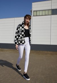 Fuzzy svartvit rutig jacka, åtsittande svart topp, vita skinny jeans och svarta platåskor med vita sulor.