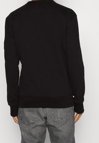 Felpa nera con maniche lunghe, polsini e orlo a costine, e una texture liscia. Indossata con jeans grigi dal design classico delle tasche.