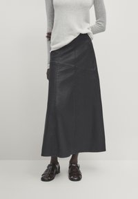 Gonna lunga in pelle nera con cuciture frontali e silhouette dritta, abbinata a sandali neri con cinturini e a un maglione grigio chiaro con texture.