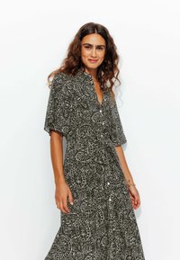 Robe longue avec un motif paisley noir et blanc, manches courtes et col. Elle présente un devant boutonné et une silhouette fluide.