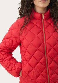 Red quilted jacket with a stand-up collar, gold zipper, and side pockets. Features diamond-shaped stitching and a soft, lightweight fabric.