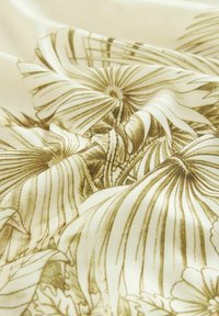 Cremefarvet stof med intrikate blomsterdesign i brune nuancer, der har teksturerede folder, som fremhæver detaljerne og dybden i designet.