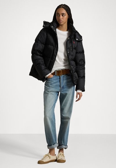 Black puffer jacket with a hood, snap buttons, and zip pockets; paired with a white shirt and light blue rolled jeans. Tan sneakers.