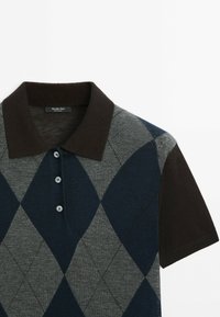 Harmaa, tummansininen ja musta argyle-tyylinen polo-paita, jossa on ruskea kaulus, lyhyet hihat ja kolme nappia. Valmistettu pehmeästä neuloksesta.