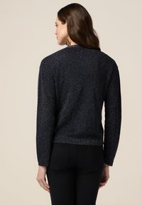 Maglione nero a maglia con un motivo testurizzato, maniche lunghe e vita aderente. Il tessuto ha una leggera lucentezza, che ne amplifica l'appeal visivo.