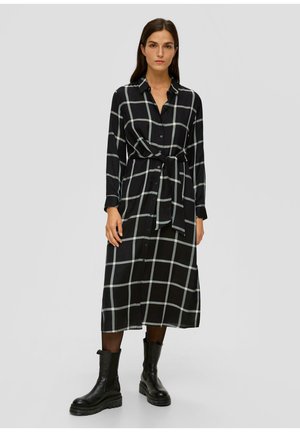 Schwarz-weiß karierte Hemdkleid mit langen Ärmeln, Taillenknoten und durchgehender Knopfleiste, kombiniert mit schwarzen Knöchelstiefeln.