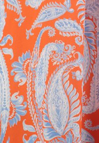 Tejido naranja adornado con intrincados patrones de paisley azul claro y espirales, que presentan formas fluidas y detalladas, así como texturas variadas.