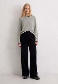 Langärmliges Oberteil mit schwarz-weißen Streifen, kombiniert mit hochtaillierten, weit geschnittenen schwarzen Cordhosen, die eine strukturierte Oberfläche und ein minimalistisches Design aufweisen.