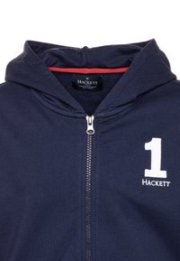 Felpa con zip color navy, cappuccio, interno rosso, ricamo bianco con "1" e "HACKETT" sul petto, e zip metallizzata.