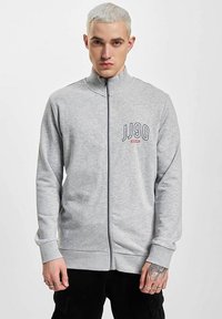 Sivá mikina na zips s vysokým golierom a rebrovanými manžetami. Na ľavej strane hrudníka je potlač "JJ90" v námorníckej modrej a červenej farbe. Textúra je z bavlneného zloženia.