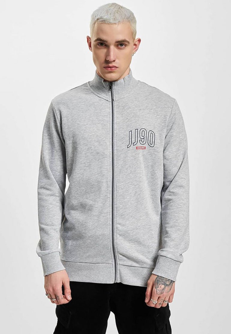 Sudadera gris con cremallera, cuello alto y puños acanalados. Presenta "JJ90" impreso en el lado izquierdo del pecho en azul marino y rojo. Textura de mezcla de algodón.