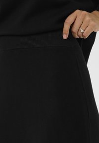 Hüve, millel on hõbesõrmus, reguleerib musta kudumise seeliku või pükste vööd inimesel, kellel on seljas sobiv must topp.