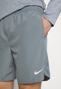 Nike miesten harmaat urheilushortsit, joissa on joustava vyötärönauha, sivutaskut ja valkoinen logo. Materiaali vaikuttaa kevyeltä ja sileältä.